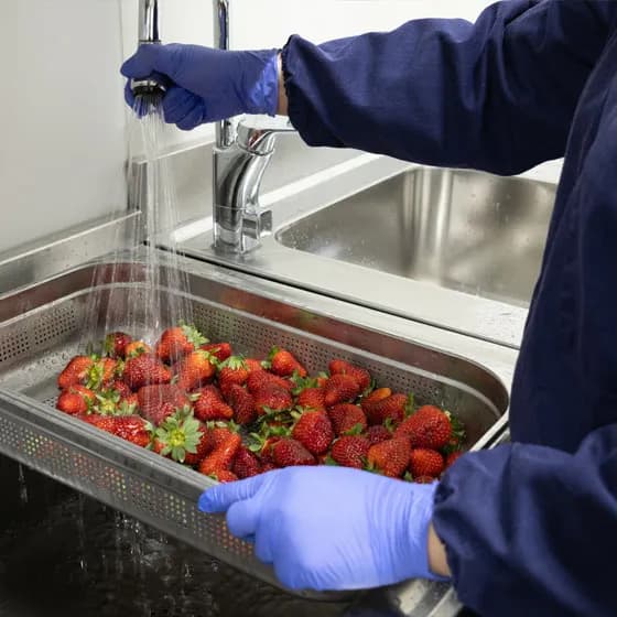 Jordgubbar sköljs under rinnande vatten i beredningsrummet