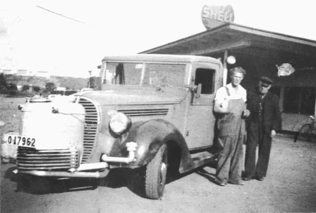 Herman Nilsson i hängslebyxor framför sin lastbil vid en Shell-mack, 1946
