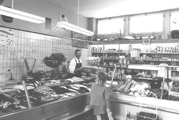 Herman Nilsson i förkläde bakom fiskdisken i butiken, med ett barn vid disken