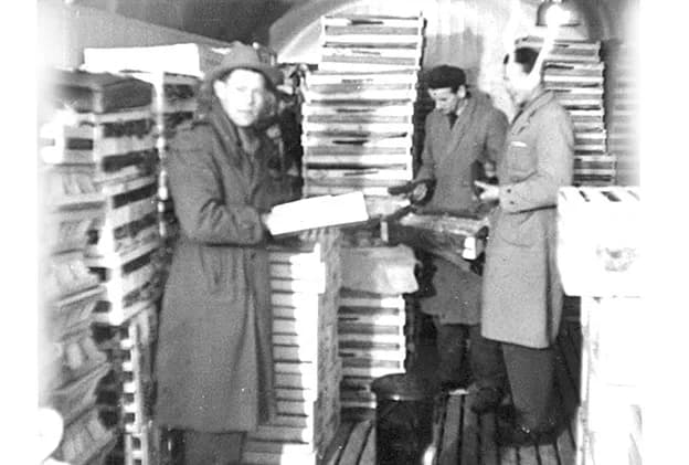 Herman Nilsson kontrollerar fraktsedlar bland staplade lådor inne i en godsvagn 1953