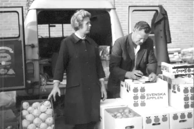 Margit och Herman Nilsson vid lådor med svenska äpplen framför en skåpbil på Partihallarna 1968