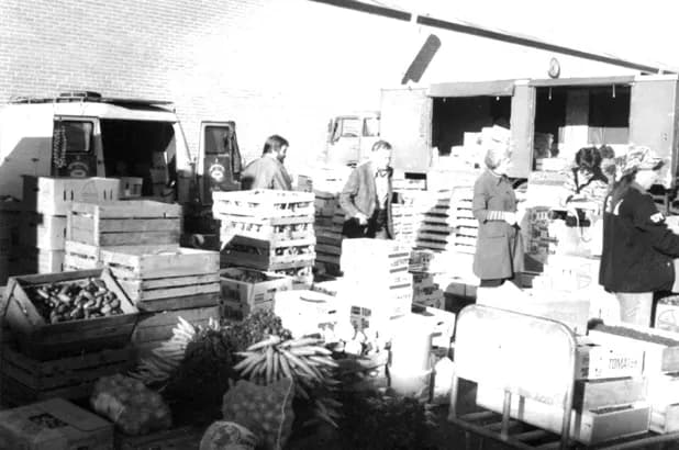 Kunder och staplade lådor med frukt och grönsaker bland bilarna på Partihallarna 1969